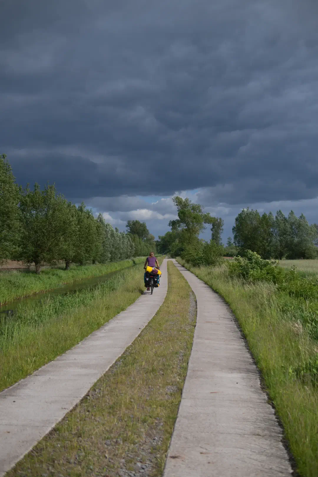 Radfahrer auf einem schmalen Betonplattenweg unter dunklen Gewitterwolken